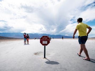 Visitantes cerca del aviso con la advertencia de calor extremo en el Valle de la Muerte.