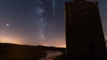 Un meteoro cruza el cielo nocturno junto a la Vía Láctea.