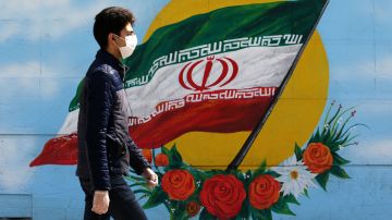 Un hombre camina ante un mural con la bandera de Irán en Teheran.
