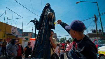 A man sprays ethyl alcohol on a figure of Saint Death as a cleaning ritual near its shrine at Alfareria street, in the Tepito neighborhood of Mexico City, on October 01, 2020. - Mexican devotees have added the protection from COVID-19 in their prayers to Saint Death. (Photo by CLAUDIO CRUZ / AFP) (Photo by CLAUDIO CRUZ/AFP via Getty Images)