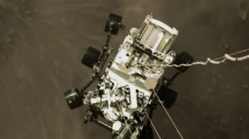 El robot Perseverance cuando estaba aterrizando en Marte, visto desde el cohete que ayudó en su descenso.