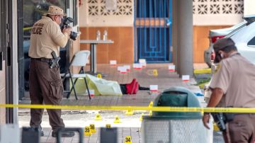 Un hombre yace en el suelo frente al salón de banquetes donde ocurrió el tiroteo masivo en Miami mientras un investigador de policía toma una fotografía.
