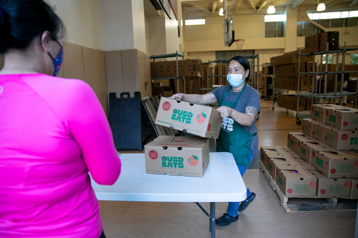 La gerente de servicio de alimentos Nakheu Saephanh entrega cajas de comida a los miembros de una familia en La Escuelita en Oakland el 7 de junio de 2021. 