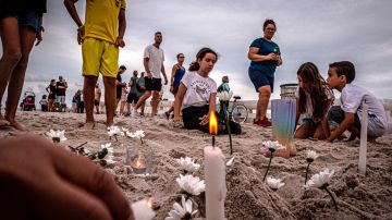 Unos niños encienden velas en una vigilia en memoria de los desaparecidos en el derrumbe del edificio en Surfside,