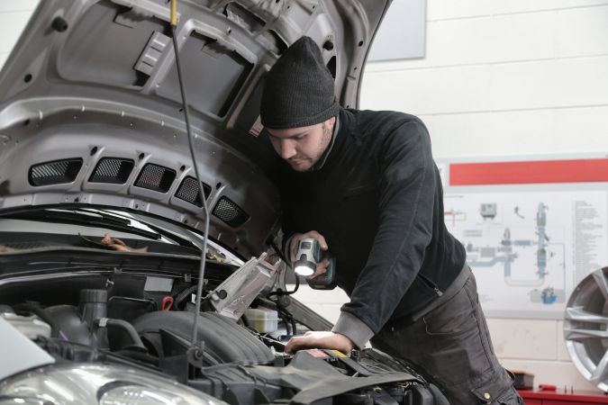 Foto de un mecánico revisando el motor del auto con una linterna