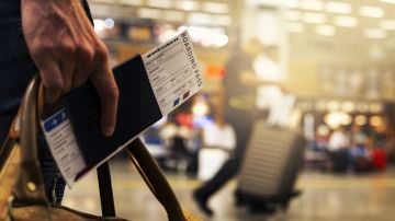 Foto de la mano de una persona sosteniendo una bolso de mano junto con su pasaporte en un aeropuerto