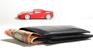 Foto de una billetera con dinero y un auto de juguete al fondo