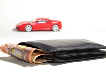Foto de una billetera con dinero y un auto de juguete al fondo