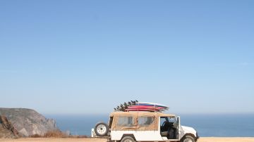 Foto de un auto cerca del mar con llevando varias tablas de surf
