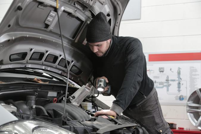 Foto de un hombre inspeccionando un auto con una linterna