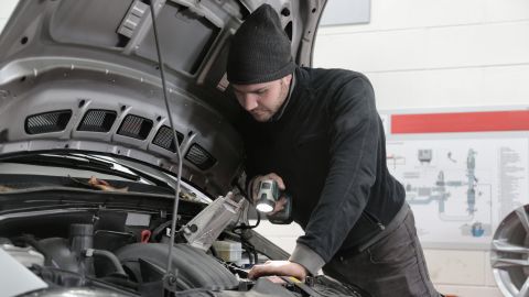 Foto de un hombre inspeccionando un auto con una linterna