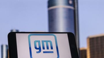Foto del logo de General Motors en un teléfono inteligente con el edificio de la compañía al fondo