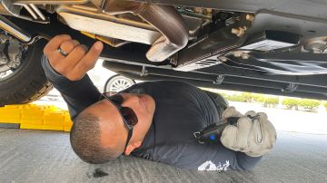 El agente del Sheriff Juan Cruz debajo de un auto mientras graba sobre un catalizador. / fotos: Jorge Luis Macías.