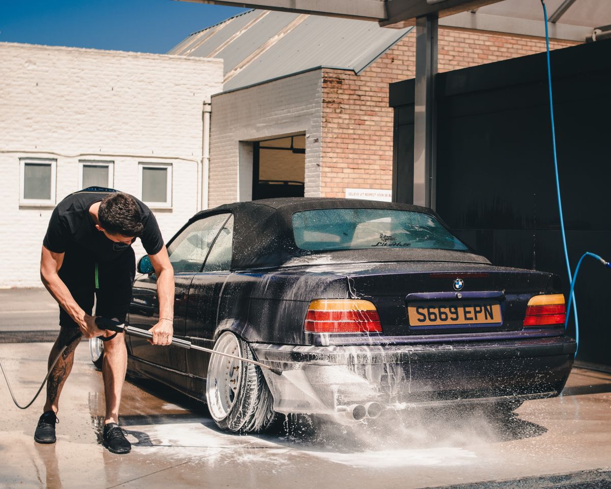 Foto de un hombre lavando su auto con una manguera