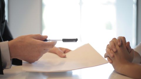 Foto de una persona entregando documentos y un bolígrafo a otra