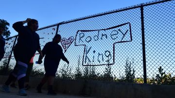 TOPSHOT - People walk past the name Rodney King seen on a chain-link fence surrounding Silver Lake Reservoir in Los Angeles, on June 9, 2020, where a new art installation protesting police brutality spells out, in colourful woven fabric, the names of unarmed African Americans who have been killed by police. - King, who was violently beaten by LAPD officers during his arrest for high speed drunk driving, became a writer after surving police brutality and died in June, 2012 from alcohol poisoning. (Photo by Frederic J. BROWN / AFP) (Photo by FREDERIC J. BROWN/AFP via Getty Images)