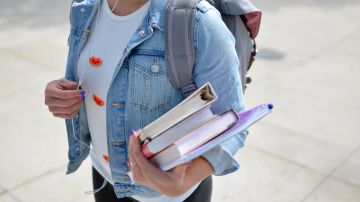 Foto de una estudiante llevando algunos libros