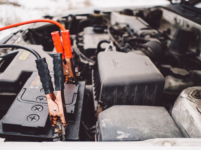 Foto de la batería de un auto conectada a unos cables auxiliares