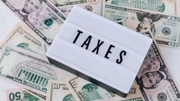 Foto de un cartel con la palabra "taxes" sobre un montón de dólares