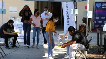 La gente espera debajo de la sombra de una carpa, luego de ser vacunada en Compton.