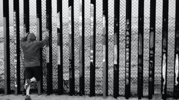 Foto de un hombre apoyado sobre el muro que limita la frontera entre Tijuana y Estados Unidos