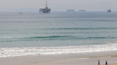 HUNTINGTON BEACH, CALIFORNIA - OCTOBER 04: People walk with a dog down a mostly empty beach a day after a 126,000-gallon oil spill from an offshore oil platform on October 4, 2021 in Huntington Beach, California. The spill forced the closure of the popular Great Pacific Airshow yesterday with authorities closing beaches in the vicinity. (Photo by Michael Heiman/Getty Images)