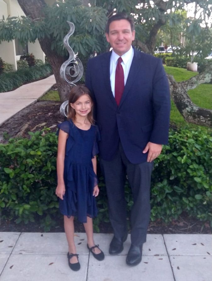 La niña Fiona Lashells junto al gobernador Ron DeSantis. / Facebook.
