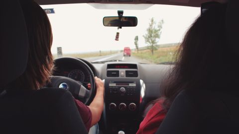 Foto de una conductora joven junto a su pasajero con la carretera al fondo