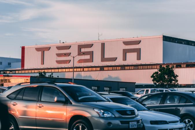 Foto de varios vehículos en un estacionamiento con una planta de Tesla al fondo