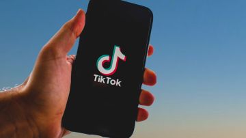 Foto de la mano de una persona con un teléfono cuya pantalla muestra el inicio de TikTok