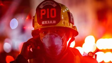 A Los Angeles Fire Department Public Information Officer wearing a facemask speaks on the phone after a fire in a single-story commercial building sparked an explosion in the Toy District of downtown Los Angeles on May 16, 2020. - At least 11 firefighters were injured in downtown Los Angeles when a fire in a commercial building sparked a major explosion and spread to nearby structures, fire officials said. Some 230 responders battled the blaze as it spread to other buildings in the area before it was extinguished around two hours after it began. (Photo by Apu GOMES / AFP) (Photo by APU GOMES/AFP via Getty Images)