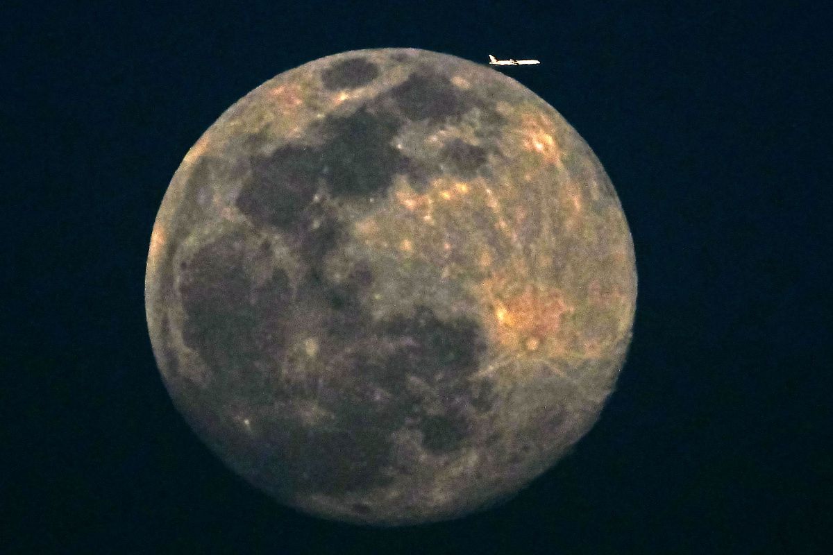 Un avión de una aerolínea comercial vuela ante la luna creciente sobre la ciudad de Kuwait.
