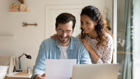 Foto de una pareja revisando unos documentos frente a una laptop