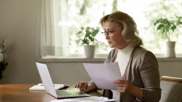 Foto de una mujer mayor frente a una laptop con documentos