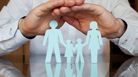 Foto de las manos de una persona sobre una figura de papel que representa a una familia