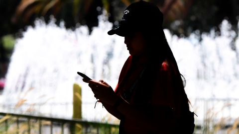 A woman uses her cellphone while walking past a water fountain in Los Angeles, California on August 13, 2019. - US retailers and global financial markets got an early Christmas present as President Donald Trump's administration announced it is delaying tariffs on key consumer electronic goods imported from China. (Photo by Frederic J. BROWN / AFP) (Photo credit should read FREDERIC J. BROWN/AFP via Getty Images)