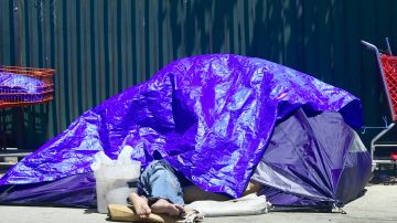 A homeless person sleeps beneath a tarp covering a tent lining sidewalks in downtown Los Angeles, California on April 20, 2017, where the city's mayor, Eric Garcetti, is proposing $176 million to help combat the city's growing homeless crisis. Los Angeles is home to one of the nation's largest homeless populations. / AFP PHOTO / Frederic J. Brown (Photo credit should read FREDERIC J. BROWN/AFP via Getty Images)