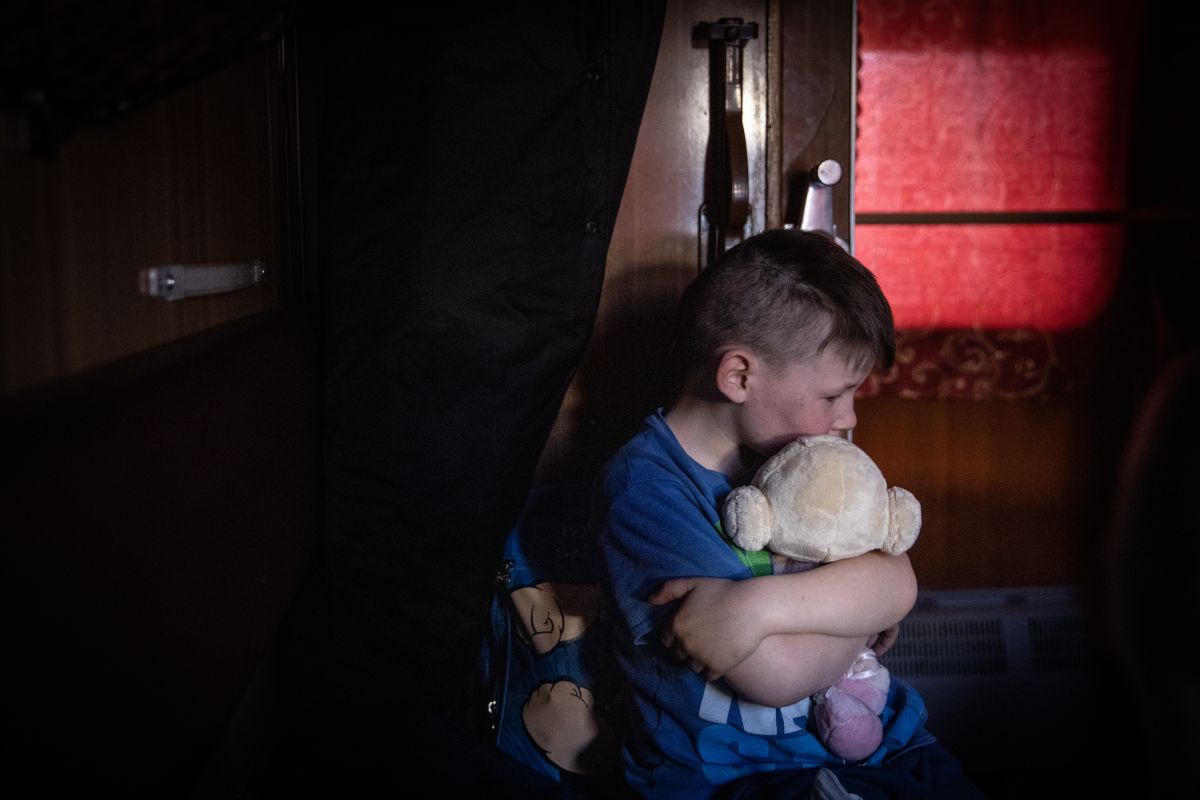 Un niño huérfano abraza un juguete y espera un tren después de huir de Polohy, en Ucrania.