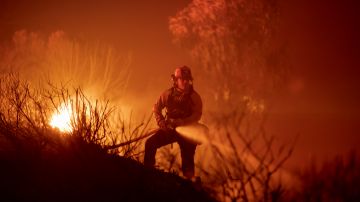 GOLETA, CA - OCTOBER 12: A firefighter hoses down a hot spot while battling the Alisal Fire at night on October 12, 2021 near Goleta, California. Pushed by high winds, the Alisal Fire grew to 6,000 acres overnight, shutting down the much-traveled 101 Freeway along the Pacific Coast. (Photo by David McNew/Getty Images)