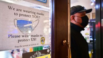 A man wears his mask as he walks past a sign posted on a storefront reminding people to wear masks, on February 25, 2022 in Los Angeles, - Los Angeles ends its indoor mask mandate on February 25 for the fully vaccinated and can show proof. The wearing of masks indoors remains for the unvaccinated and fail to show proof of a negative test. (Photo by Frederic J. BROWN / AFP) (Photo by FREDERIC J. BROWN/AFP via Getty Images)