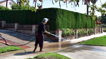 A woman waters down her driveway in Monterey Park, California on April 27, 2022, a day after Southern California delared a water shortage emergency with unprecedented new restrictions on outdoor watering for millions of people living in Los Angeles, San Bernardino and Ventura counties. - Southern California's Metropolitan water district will allow for outdoor watering tp just one day per week effective June 1st. (Photo by Frederic J. BROWN / AFP) (Photo by FREDERIC J. BROWN/AFP via Getty Images)