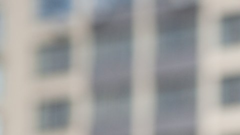 La mano de una persona que extiende las llaves de una vivienda con unos departamentos en el fondo.