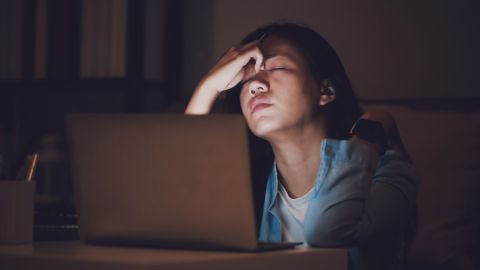 una persona agotada con la mano en el rostro y frente a una computadora.