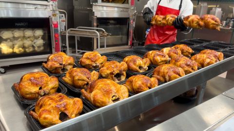 Varios pollos rostizados formados sobre una plancha y un hombre que manipula una lanza con pollos.