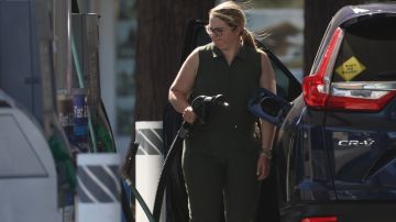 una mujer sostiene una manguera para cargar gasolina en una estación de servicio.