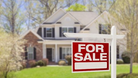 El letrero de venta de una vivienda en un jardín y una casa en el fondo.