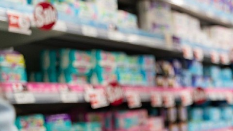 Una persona empuja un carro de supermercado por un pasillo lleno de productos.
