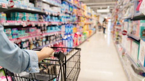 Una persona empuja un carro de supermercado por un pasillo lleno de productos.