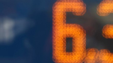 Imagen de una torre de precios y en el fondo el conductor de un vehículo.