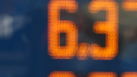 Imagen de una torre de precios y en el fondo el conductor de un vehículo.